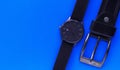 Wrist black watch and plaque from a black leather belt on a blue background. Men`s Accessories. View from above.