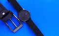 Wrist black watch and plaque from a black leather belt on a blue background. Men`s Accessories. View from above.