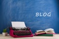 writer's workplace - typewriter and books on blue blackboard background with text "Blog