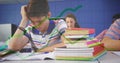 Writing boy in striped shirt leaning over notebook in classroom, with textbook stacks, chart lines Royalty Free Stock Photo