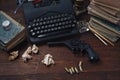 Writing a crime fiction story - old retro vintage typewriter and revolver gun with ammunitions, books, papers, old ink pen