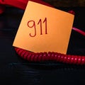 Writing 911 on memo post reminder.  sticky paper surrounded by wire of landline phone Royalty Free Stock Photo