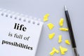 Writing a motivational phrase LIFE IS FULL OF POSSIBILITIES. Business concept desktop with notepad pen scraps of paper on a