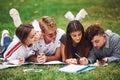 Writing on paper. front view. Group of young students in casual clothes on green grass at daytime