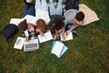 Writing on paper. With laptop. Group of young students in casual clothes on green grass at daytime