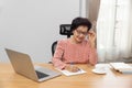 Writing After Retirement. Asian senior woman writer is writing details on book while working on laptop at home Royalty Free Stock Photo