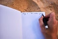 Human hand holding a pen and writing notes in a travel journal diary in the sand on white paper. Royalty Free Stock Photo