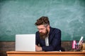 Writing school report. Teacher bearded hipster with eyeglasses sit in classroom chalkboard background. School teacher