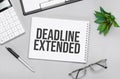 Writing text showing deadline extended. Calculator,pen,plan,glasses and black folder on grey background