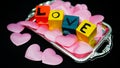 Written LOVE on colored wooden cubes with pink cloth hearts on a silver plastic tray Royalty Free Stock Photo