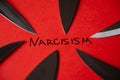 Written Narcisism, in black on a red sheet, with knife blades next to it Royalty Free Stock Photo