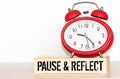 Written pause reflect with paper on alarm clock. Pause and reflect word with time concept.