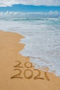 2020 2021 written in the sand with a wave erasing 2020