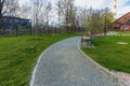 Small green square with wooden benches, bushes, trees and river behind new and modern estate