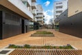 Small path between modern buildings of new estate with dark facades and big bushes in center with