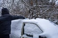 A man cleaning snow from car roof in winter. Classic Mercedes Benz 190D.