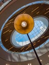 Looking up to round hanging lamp in front of ceiling and skylight of shopping mall