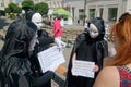 Three actors, dressed in white theater masks and black cloaks, entertain people at a festive fair on a city street