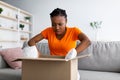 Wrong parcel. Frustrated Afro woman unpacking carton box, unhappy with bad delivery service, sitting on couch at home Royalty Free Stock Photo