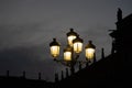 Wrought iron lamp with five lanterns dimly illuminating with yellow light at dusk in the main square of Salamanca with the gray