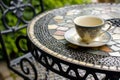 wrought iron table with mosaic tiles, empty teacup, and saucer