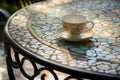 wrought iron table with mosaic tiles, empty teacup, and saucer