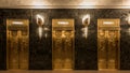 16x9 crop of elevators in vintage art deco building with marble walls and golden sconces
