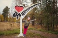 'I love Michurinskoye village' written on a pole and happy patriotic russian girl stretching her arms against