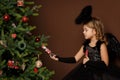 X-mas, winter vacation and people concept - little girl in black angel costume sits on a trunk near a Christmas tree and looks at Royalty Free Stock Photo