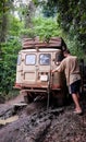 4x4 offroad vehicle stuck on muddy dirt road with young man trying to recover it in rain forest of Cameroon, Africa Royalty Free Stock Photo