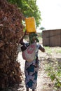 Woman collecting water in container and carried balanced on head with child in a capulana on her back