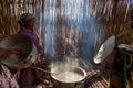 Women preparing food in a rough kitchen with stick walls and a log fire with smoke rising