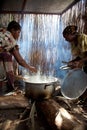 Women preparing food in a rough kitchen with stick walls and log fire.