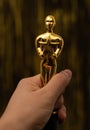 Woman hand holding a plastic Oscar award on golden background