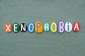 Xenophobia, creative word composed with multi colored stone letters over green sand