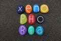 Xenophobia, social issue concept word composed with colored stones over black volcanic sand