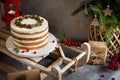 Xmas cake decorated with rosemary and cranberries on wooden sledge with christmas tree and presents on the background. Bakery,