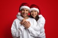 Xmas Couple. Man And Woman Wearing Santa Hats Embracing On Red Background