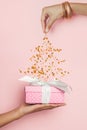 Xmas gift and Christmas tree made from falling golden confetty stars on pastel pink background Royalty Free Stock Photo