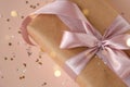 Xmas gift package in kraft paper with pink ribbon on trendy natural beige background with glitter. Zero waste pack
