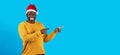 Xmas Offer. Cheerful Black Guy In Santa Hat Pointing At Copy Space