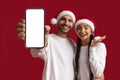 Xmas Offer. Excited Young Arab Couple In Santa Hats Demonstrating Blank Smartphone