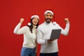 Xmas offer. Overjoyed arab couple in Santa hats celebrating success with laptop computer, standing over red background
