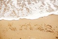 Xmas text written on sandy beach with wave near sea. Travel and Royalty Free Stock Photo