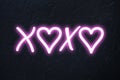 xoxo written in pink neon style with hearts on black background