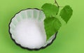 Xylitol birch sugar in bowl with birch leaves over green Royalty Free Stock Photo