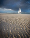 A yacht sailing with storm clouds over head and wet golden sands in the foreground