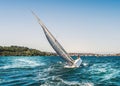 A Yacht tilting, heeling in the water it has a large silver grey sail and is cutting through the blue water of Sydney harbour.