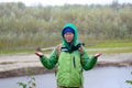 Yakut Asian girl tourist in a jacket hat and hood and with a backpack is closing his eyes, under the hail and rain.