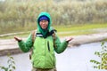 Yakut Asian girl tourist in a jacket hat and hood and with a backpack is smiling, hail and rain holding up his hands